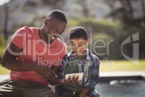 Son and father using mobile phone near poolside