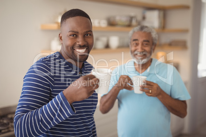 Smiling father and son having cup of coffee in kitchen