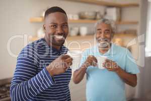 Smiling father and son having cup of coffee in kitchen