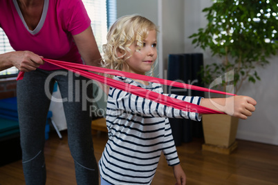 Physiotherapist assisting girl patient in performing stretching exercise with resistance band