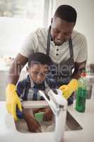 Smiling father and son cleaning utensils in kitchen