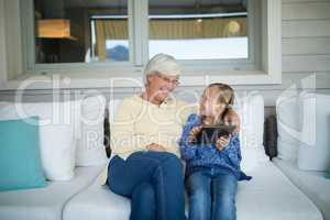 Smiling granddaughter and grandmother using digital tablet on sofa