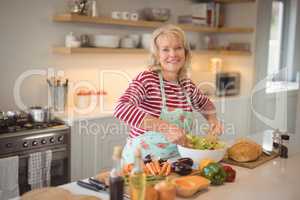 Senior woman mixing vegetables salad in kitchen