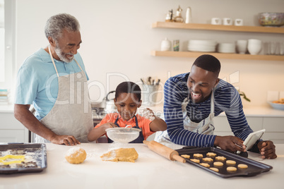 Boy preparing cookie dough with his father and grandfather in kitchen