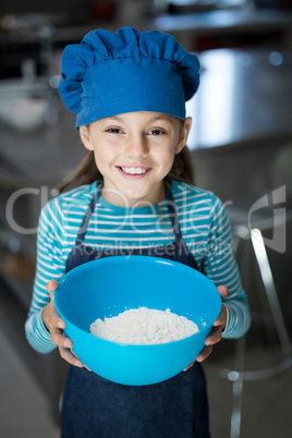 Smiling girl holding a bowl of flour in the kitchen