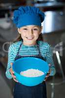 Smiling girl holding a bowl of flour in the kitchen