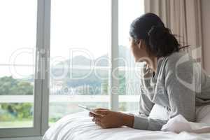 Woman looking away while holding digital tablet on bed