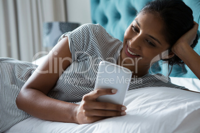 Smiling woman using phone while relaxing on bed