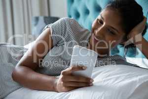 Smiling woman using phone while relaxing on bed