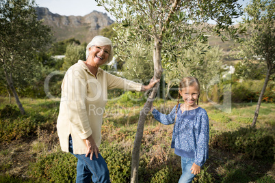 Smiling granddaughter and grandmother standing together in garden