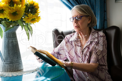 Senior woman reading book while sitting in retirement home