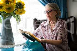 Senior woman reading book while sitting in retirement home