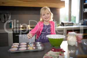 Smiling girl pouring cupcake batter