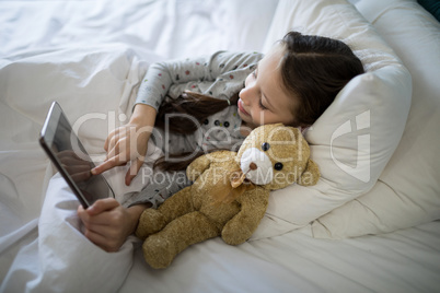 Girl using digital tablet while lying on bed