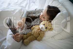 Girl using digital tablet while lying on bed