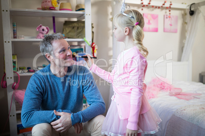 Cute daughter in fairy costume putting makeup on her fathers face