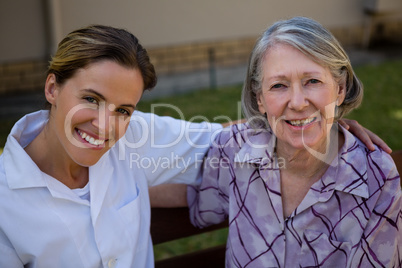Portrait of happy senior woman and doctor sitting on bench