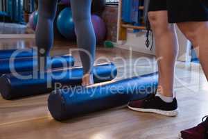 Physiotherapist assisting senior woman in performing exercise on foam roll