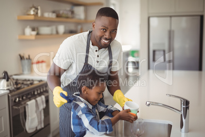 Smiling father and son cleaning cup in kitchen