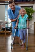 Physiotherapist assisting girl patient to walk with crutches