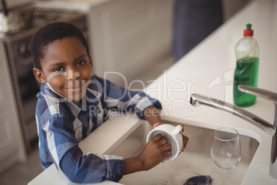 Smiling boy washing cup in kitchen sink