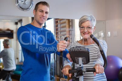 Physiotherapist assisting senior woman on exercise bike