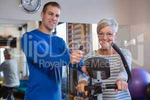 Physiotherapist assisting senior woman on exercise bike