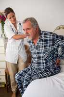 Doctor assisting senior patient in sitting on bed at nursing home