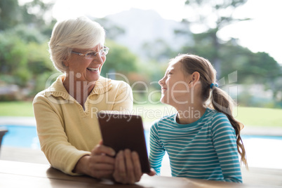 Grandmother and granddaughter talking over a digital tablet near the pool