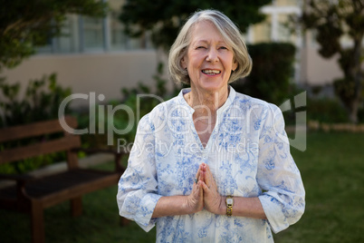 Portrait of happy senior woman standing in prayer position
