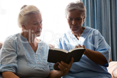 Doctor with senior woman reading book while sitting in retirement home