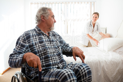 Senior man looking at doctor adjusting bed while sitting on wheelchair