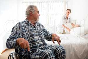 Senior man looking at doctor adjusting bed while sitting on wheelchair