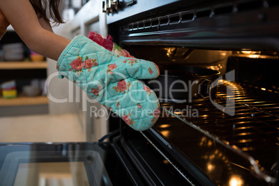 Cropped hands of girl wearing glove putting container with cake in oven