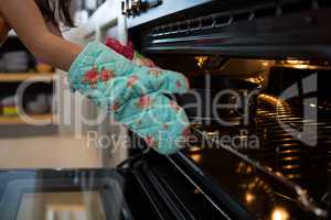 Cropped hands of girl wearing glove putting container with cake in oven