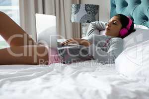 Relaxed woman listening to music while using laptop on bed