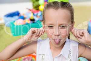 Close up portrait of girl holding ears while sticking out tongue