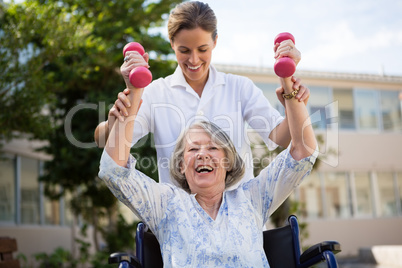 Doctor assisting woman in lifting dumbbells at park Doctor assisting woman in lifting dumbbells at park