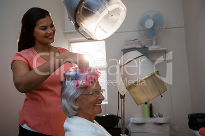 Smiling beautician removing curlers from senior woman hair
