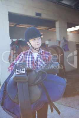 Teenage girl holding horse equipments in the stable