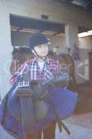 Teenage girl holding horse equipments in the stable