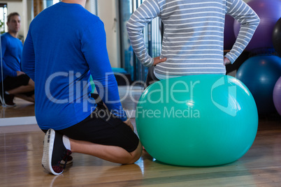 Physiotherapist assisting senior woman on exercise ball at clinic