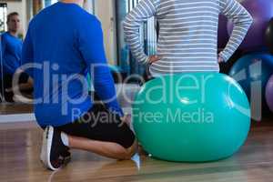 Physiotherapist assisting senior woman on exercise ball at clinic