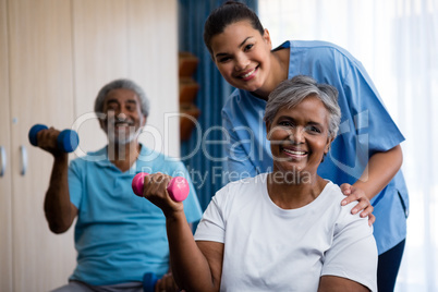 Portrait of nurse training seniors in lifting dumbbells