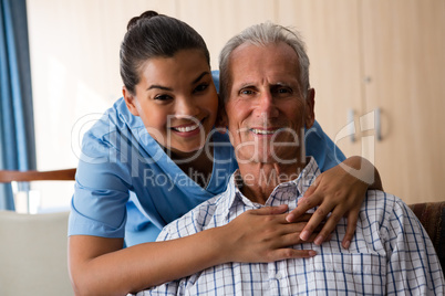 Smiling female doctor standing by senior man sitting in nursing home