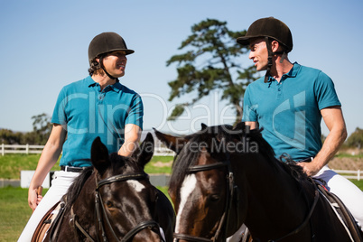 Two male jockeys riding horse in the ranch