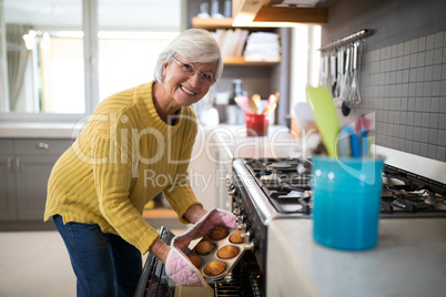 Senior woman taking tray of fresh cookies out of oven in kitchen