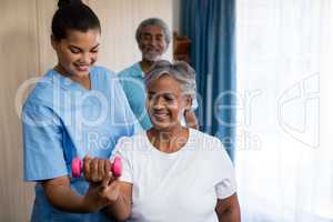 Nurse guiding senior woman in lifting dumbbell