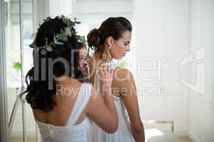 Bridesmaid assisting bride to dress