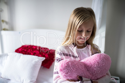 Girl holding heart shape pillow on bed